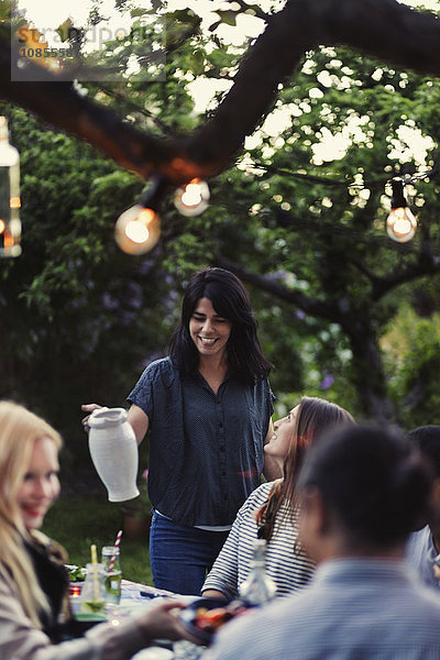 Smiling woman holding jug while friends sitting at dining table during party