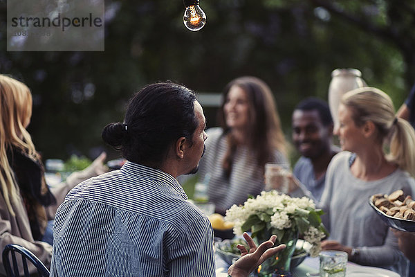 Rear view of man sitting at dining table with friends at outdoor dinner party