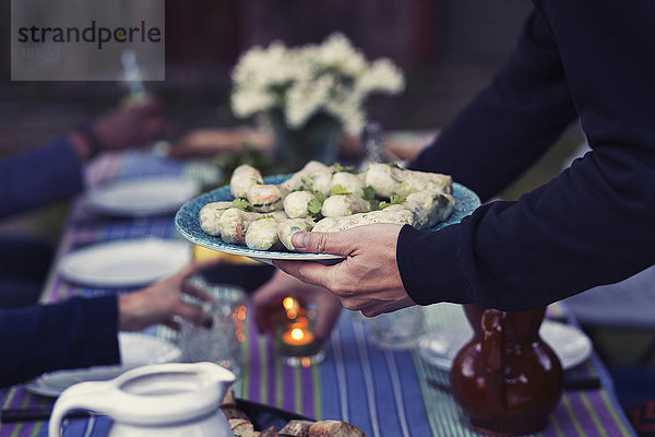 Cropped image of man holding plate with rice paper rolls at outdoor food table during party