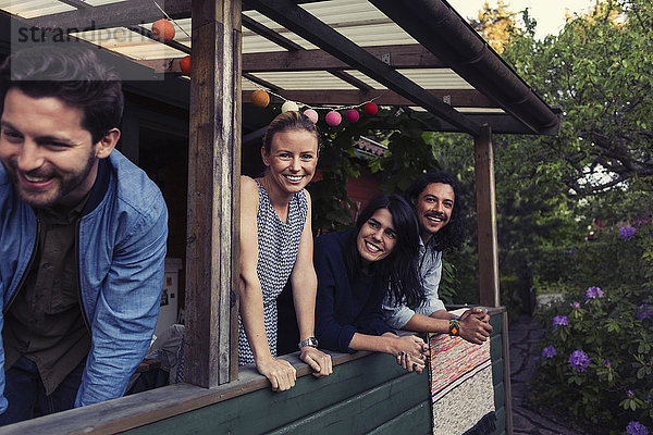 Portrait of happy young woman standing with friends on porch at log cabin