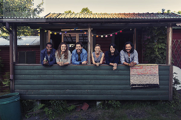 Portrait of happy multi-ethnic friends standing on porch at log cabin