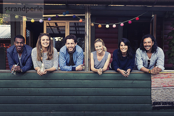 Portrait of multi-ethnic friends standing on porch at log cabin