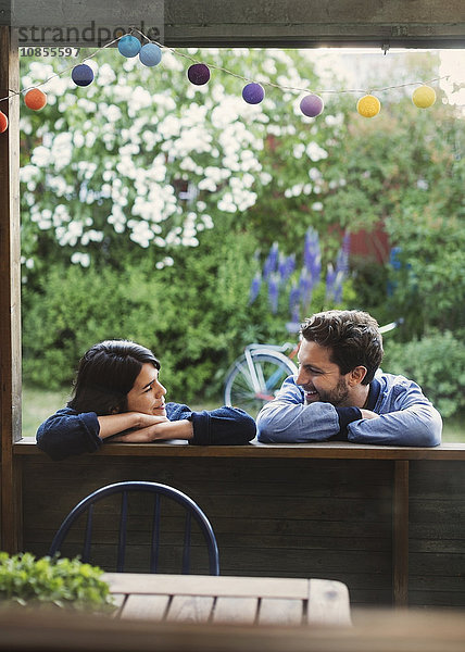 Smiling couple looking at each while leaning on log cabin