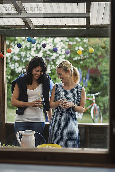 Happy female friends holding drink bottles while standing in log cabin during party