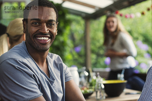 Portrait of happy man sitting with friends at porch in summer house