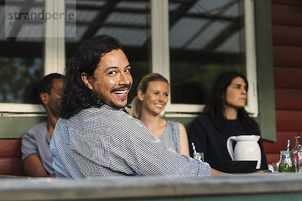 Rear view portrait of happy man sitting with friends at log cabin