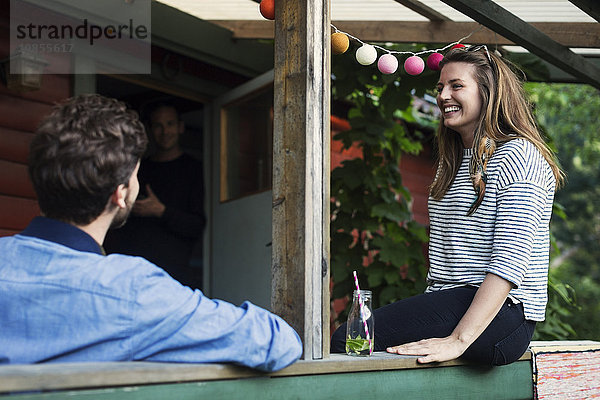 Happy woman sitting with friend at porch in log cabin