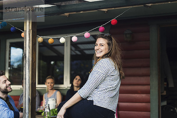 Side view portrait of happy woman sitting with friends in log cabin