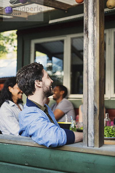 Side view of happy man sitting at porch while enjoying summer party with friends