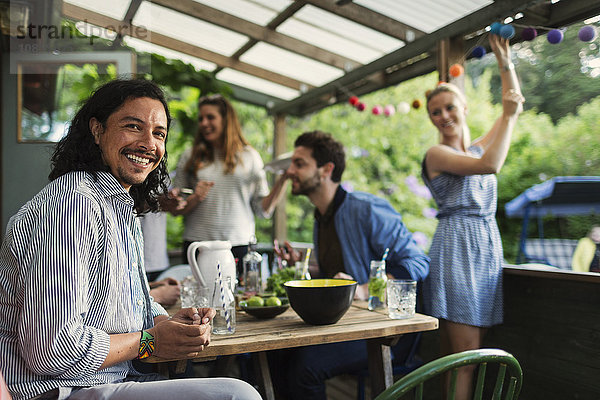 Portrait of happy man sitting at table while enjoying party with friends at summer house