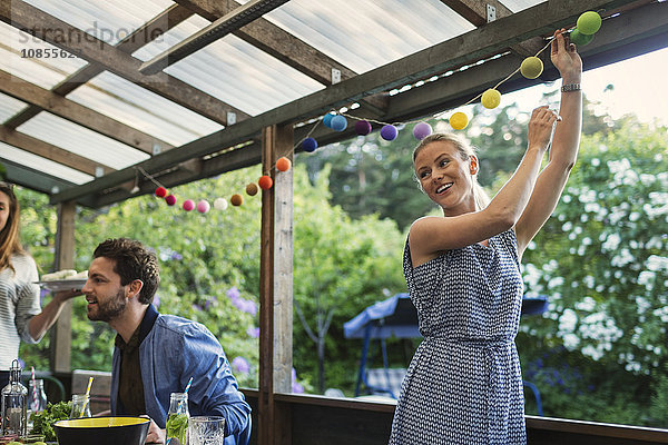 Happy young woman decorating log cabin during summer party with friends