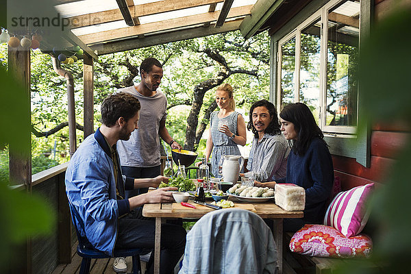 Multi-ethnic friends having food on porch at log cabin during summer party