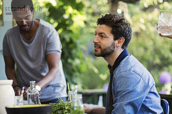 Side view of man sitting on porch at log cabin during summer party