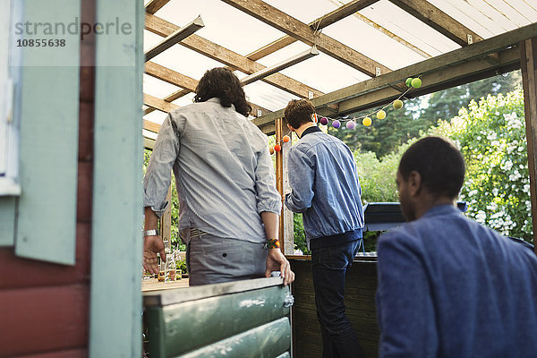 Rear view of male friends entering log cabin during summer party