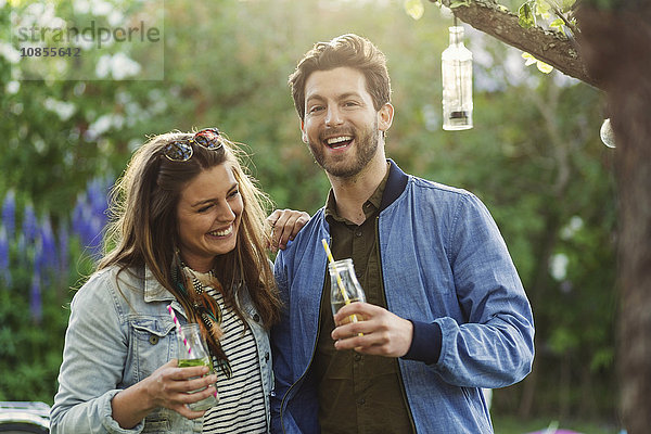 Portrait of happy man enjoying with woman while holding drink bottles at summer party