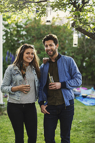 Portrait of happy couple holding drink bottles at summer party