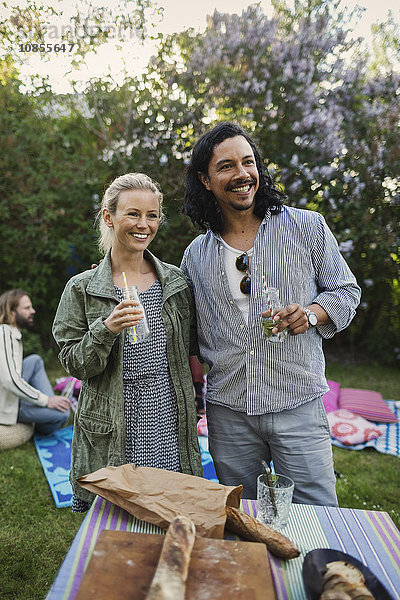 Happy couple looking away while holding drink bottles at summer party