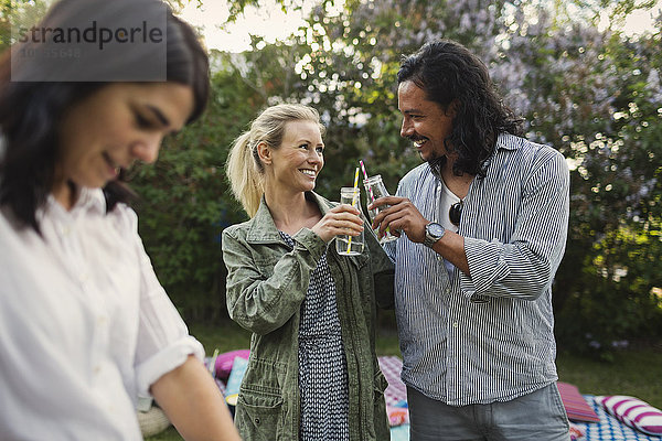 Happy couple toasting drink bottles during summer party in yard