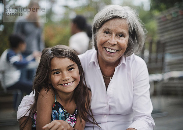 Portrait of happy grandmother sitting with granddaughter at yard