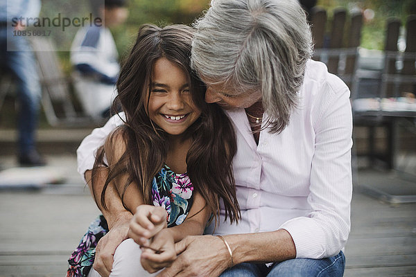 Senior woman embracing granddaughter while sitting at yard