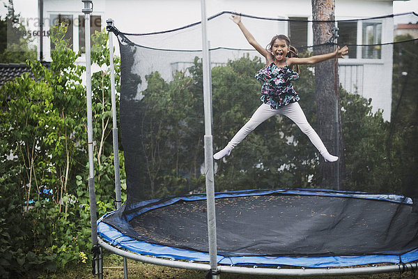 Portrait of excited girl jumping on trampoline at yard