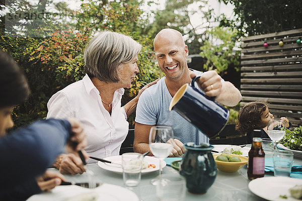 Happy man serving water to mother at outdoor dining table