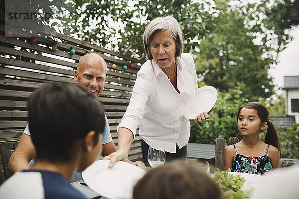 Senior woman giving plate to grandson at outdoor dining table