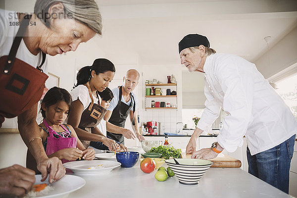 Senior man guiding family in preparing Asian food at kitchen