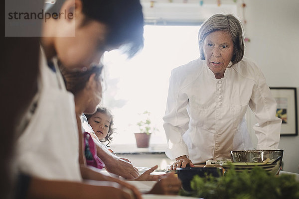 Senior woman guiding family to in making Asian food in kitchen