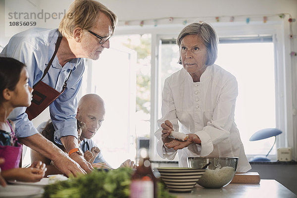 Senior woman teaching family to make Asian food in kitchen