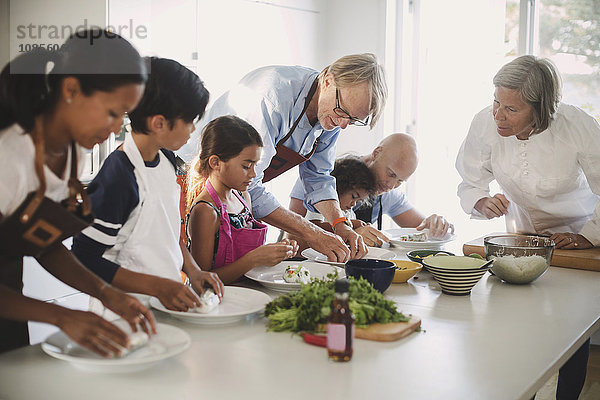 Senior woman guiding family in preparing Asian food in kitchen