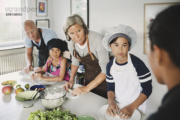 Family looking at woman while preparing food in kitchen