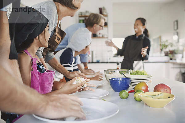 Happy woman talking to family preparing food at table in kitchen