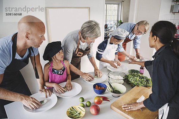 Woman guiding multi-generational family in preparing Asian food at kitchen