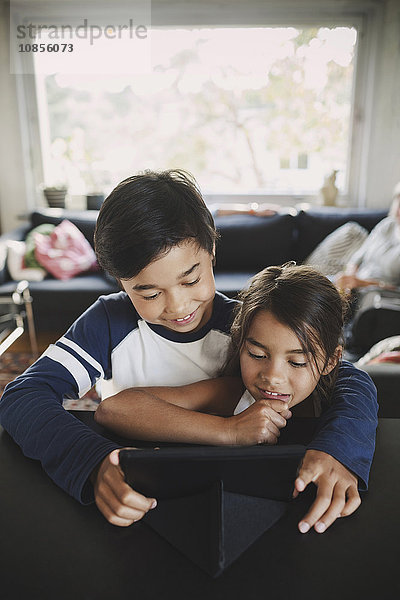 Happy siblings using digital tablet at home