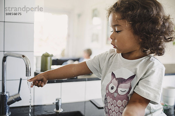 Girl washing hand under faucet in kitchen