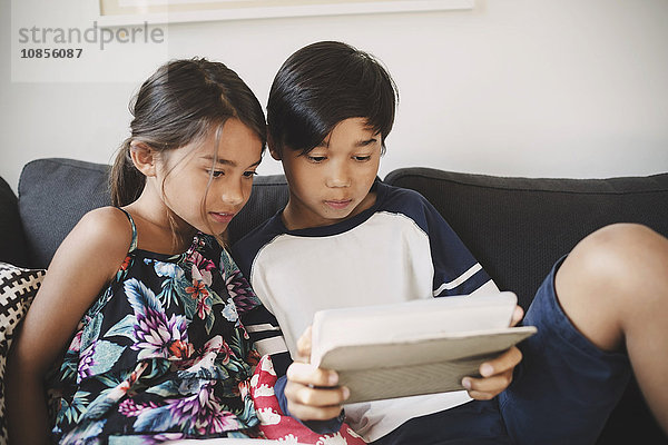 Brother and sister using digital tablet while sitting on sofa at home