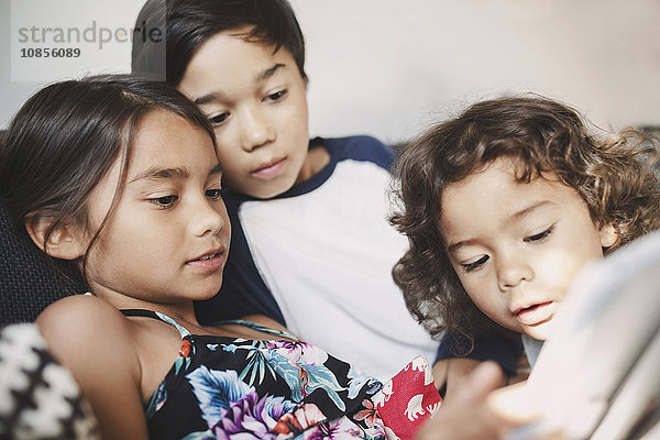 Brothers and sister using digital tablet on sofa at home