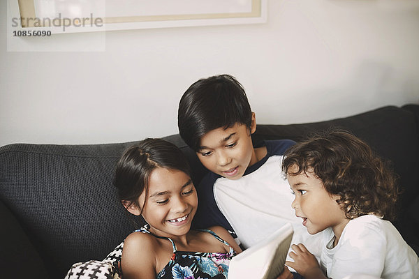 Siblings using digital tablet on sofa at home