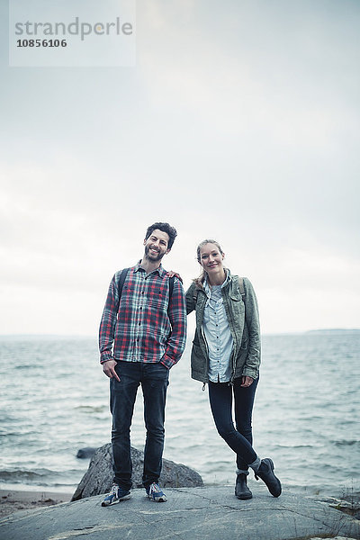 Full length portrait of confident wonderlust couple standing on rock by sea