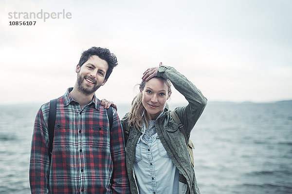 Portrait of confident wonderlust couple standing against sea