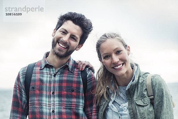 Portrait of happy wonderlust couple standing against sky