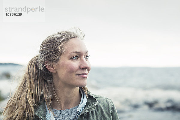 Smiling young woman looking away by sea against sky