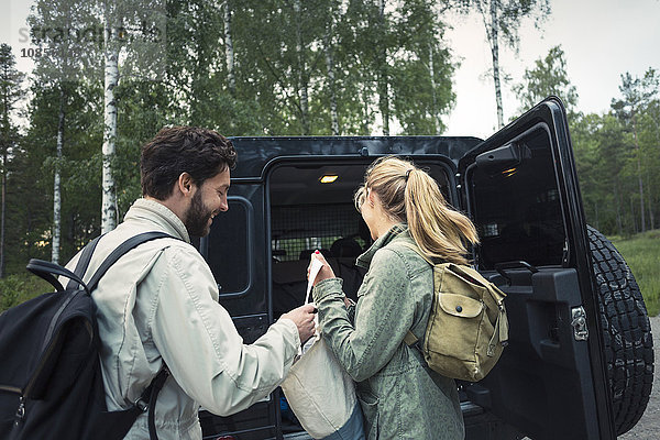 Side view of wonderlust couple unloading bag from jeep at countryside