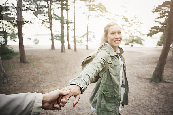 Happy woman holding man's hand in forest