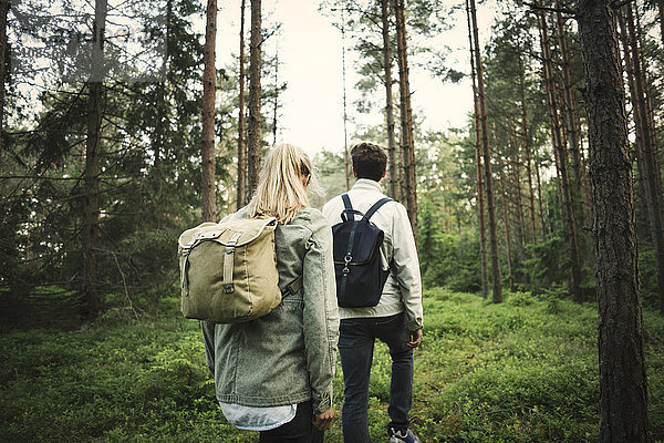 Rear view of couple carrying backpacks while walking through forest