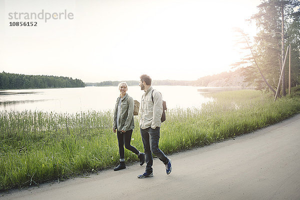 Full length of happy wonderlust couple walking on road by lake against clear sky