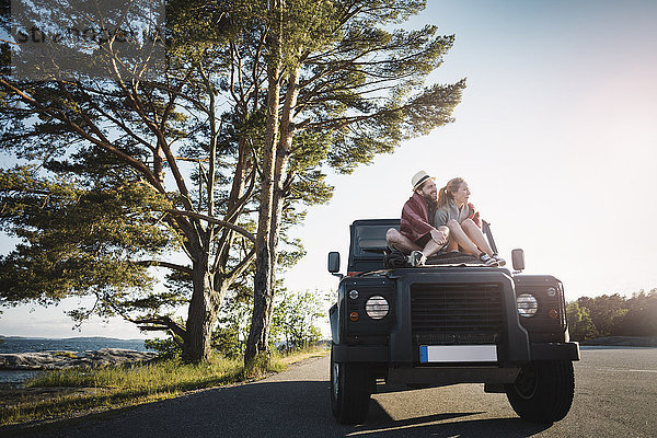 Couple sitting on jeep at countryside