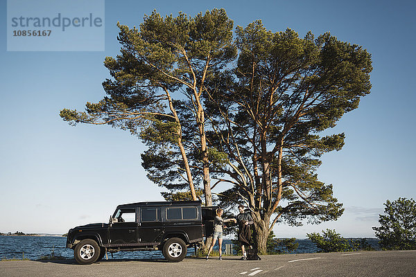 Couple standing outside jeep at lakeshore against blue sky