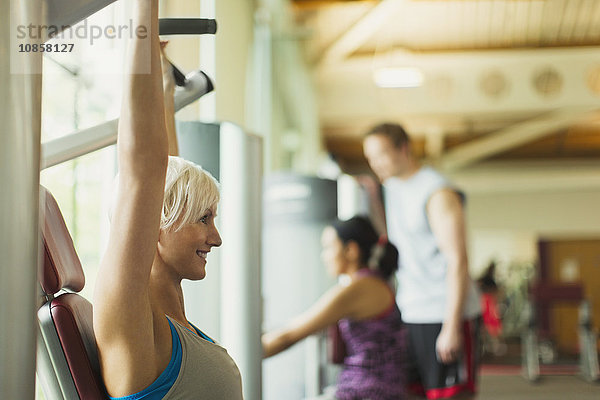 Lächelnde Frau mit erhobenen Armen mit Trainingsgeräten im Fitnessstudio